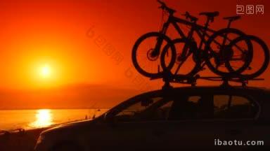 汽车的剪影与自行车安装在夏天的海滩上日落